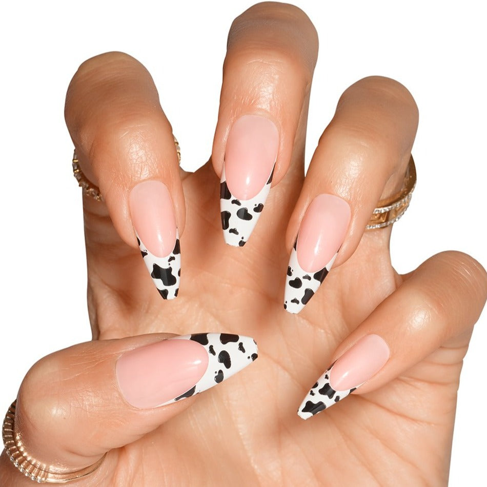 Hand in claw pose wearing cow printed French tip stick on nails