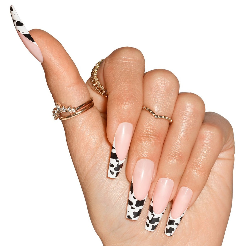 Hand wearing Big Moood nails, natural french with cow print on tip, in coffin shape ultra long length